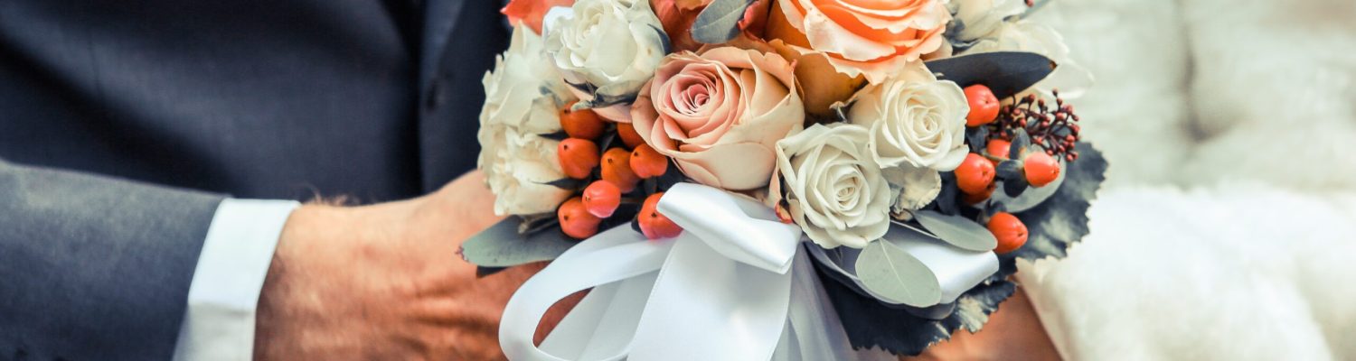 A selective focus closeup shot of a wedding couple holding a flower bouquet with white and orange roses